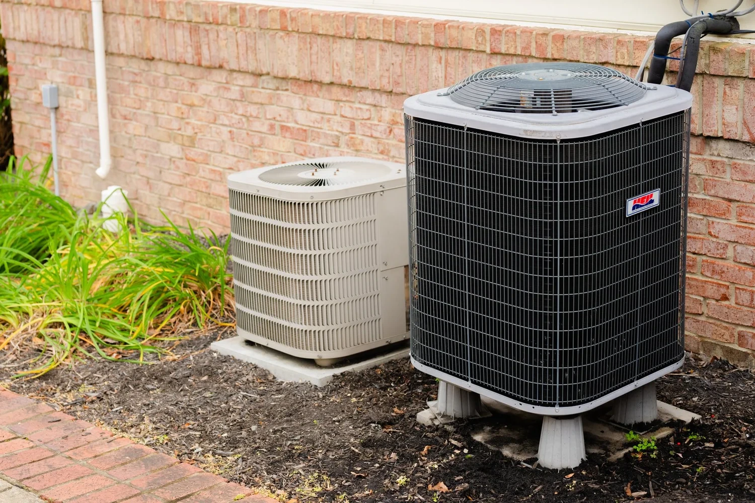 Two outdoor condensing units on pads beside a brick house